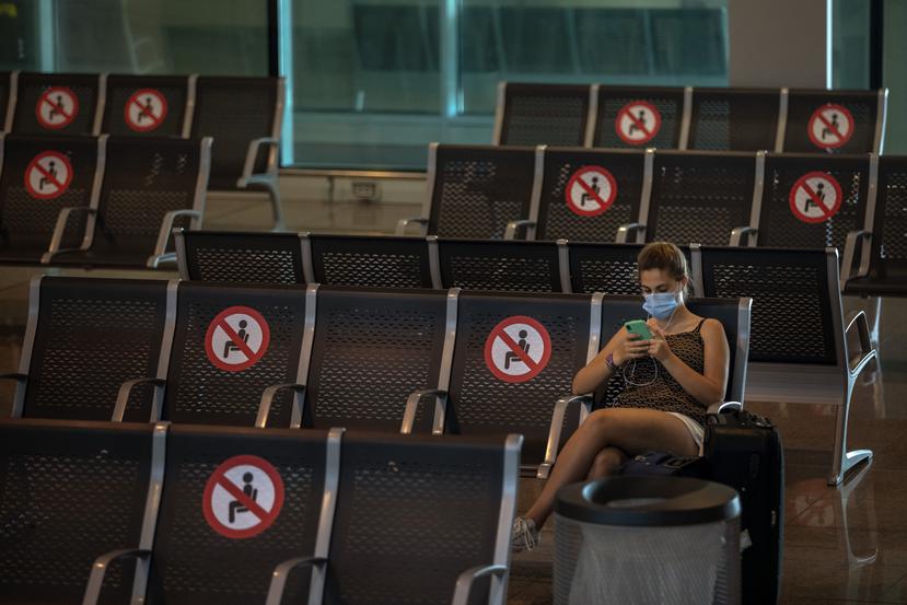 Una mujer mira su celular en una sala de espera del aeropuerto de Barcelona el 30 de junio del 2020. Carteles en los respaldos evitan que la gente se siente una al lado de la otra.