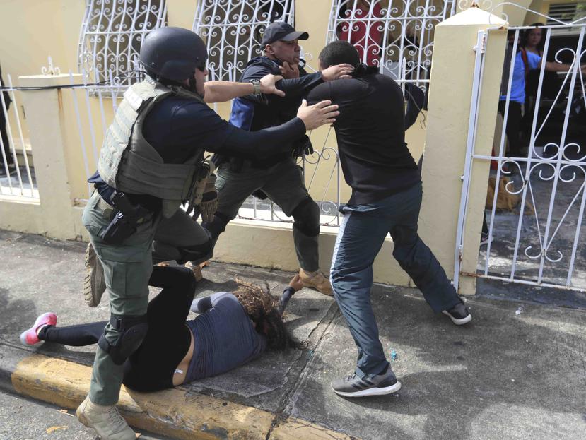 Dos agentes de la Policía estatal intentan detener a un manifestante mientras una mujer busca no ser pisoteada.
