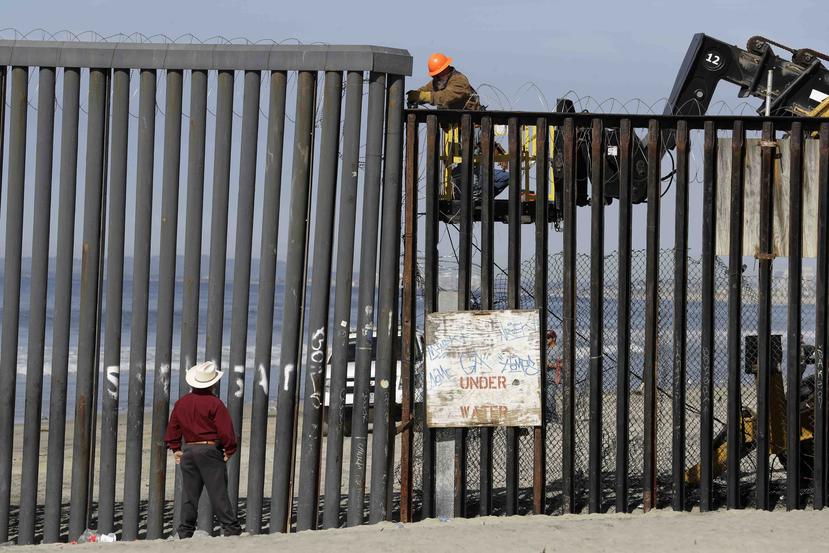 Un hombre en el lado estadounidense de la frontera (arriba) trabaja en la estructura ante la mirada de otro desde la playa, en Tijuana, México. (AP)
