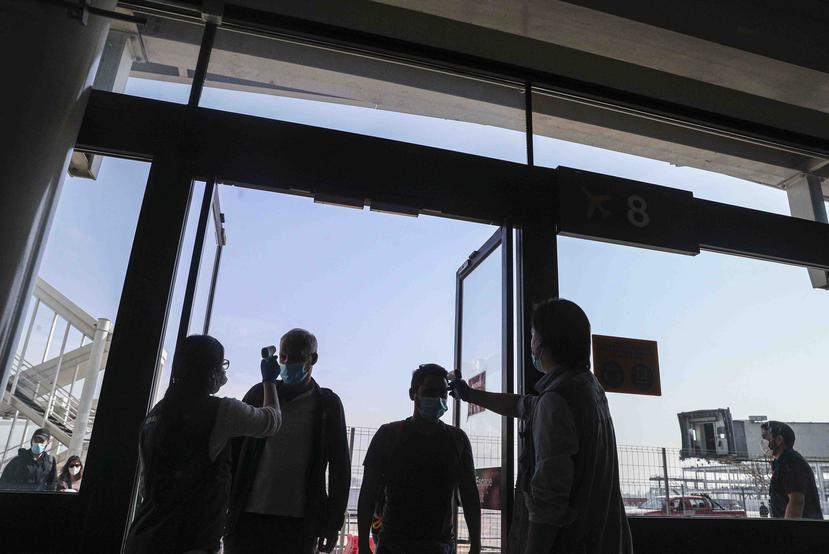 Trabajadores de la salud le miden la temperatura a los chilenos después de aterrizar en el aeropuerto Arturo Merino Benítez, en Santiago. (AP / Esteban Félix)