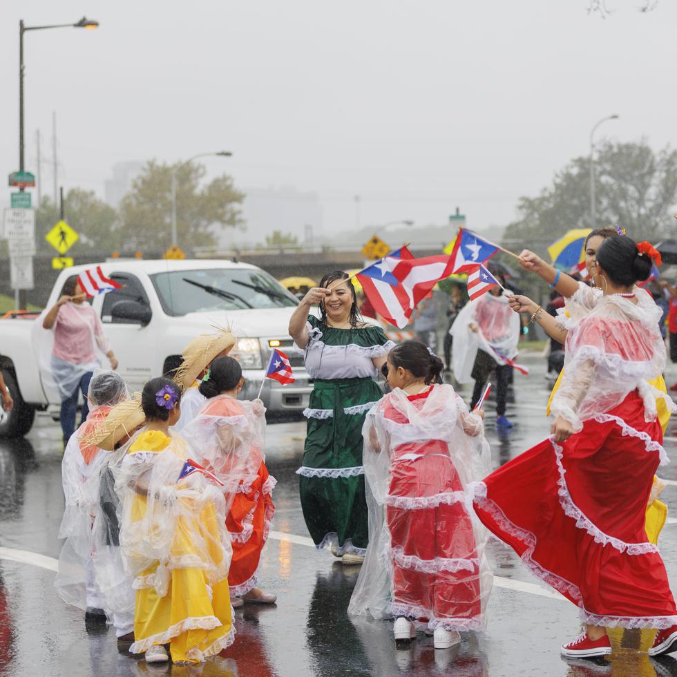 Varias niñas y niños vestidos con trajes típicos bailan bajo la lluvia durante la parada celebrada esta tarde.