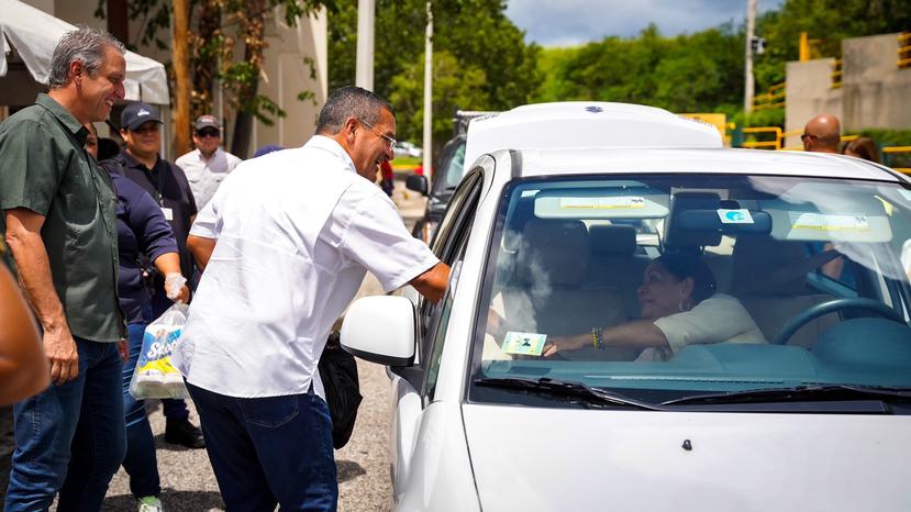 El gobernador Pedro Pierluisi saluda a una persona durante un recorrido por el pueblo de Coamo, izquierda.