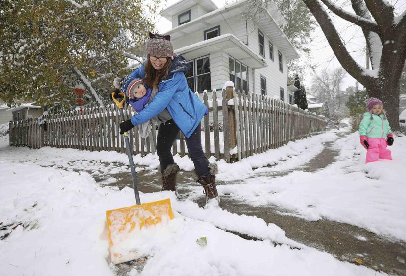 Stephanie Rytilahti limpia la vereda de su casa que se llenó de nieve tras una nevada mientras carga a su hijo de un año, Orion, en Madison, Wisconsin. (Amber Arnold/Wisconsin State Journal via AP)