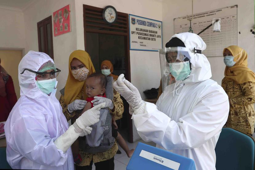 Trabajadores de la salud con trajes protectores se preparan para administrar la vacuna del sarampión a un bebé en un centro comunitario en Tangerang, Indonesia, el martes 12 de mayo de 2020. (AP)