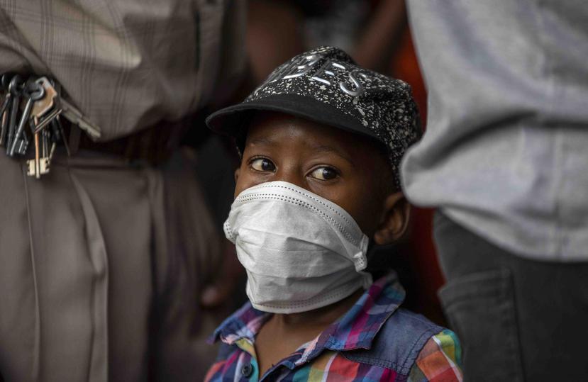 Un niño utiliza una mascarilla para protegerse contra el coronavirus mientras su padre está formado en una tienda en Soweto, Sudáfrica. (AP)