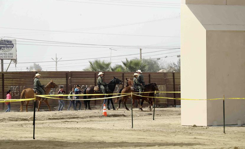 Un grupo de personas detenidas por agentes a caballo de la Patrulla Fronteriza tras cruzar de forma ilegal a territorio estadounidense desde Tijuana, México, pasa junto a los prototipos de muro fronterizo, a la derecha, que se están construyendo en San Di
