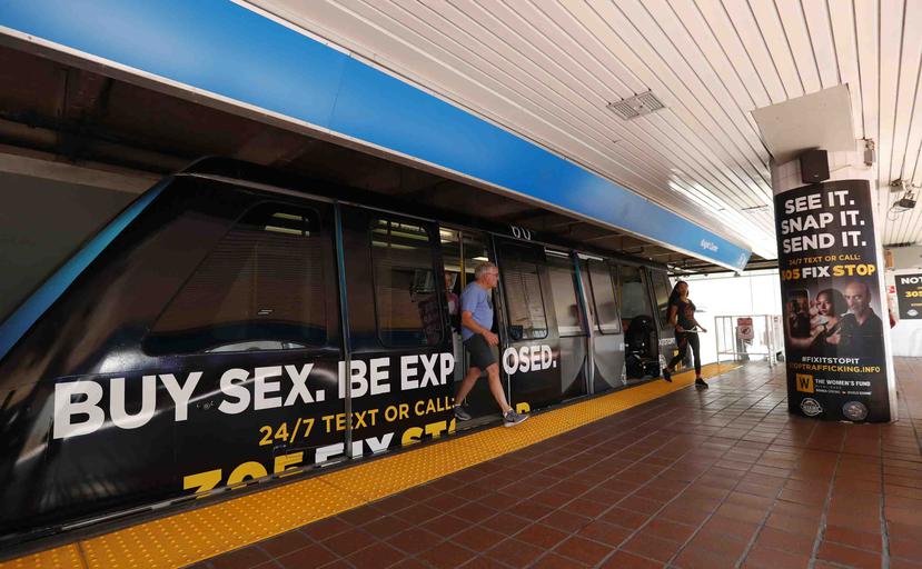 Dos personas salen de un tren urbano cubierto con afiches contra el tráfico sexual, el miércoles 6 de noviembre de 2019, en Miami. (AP)