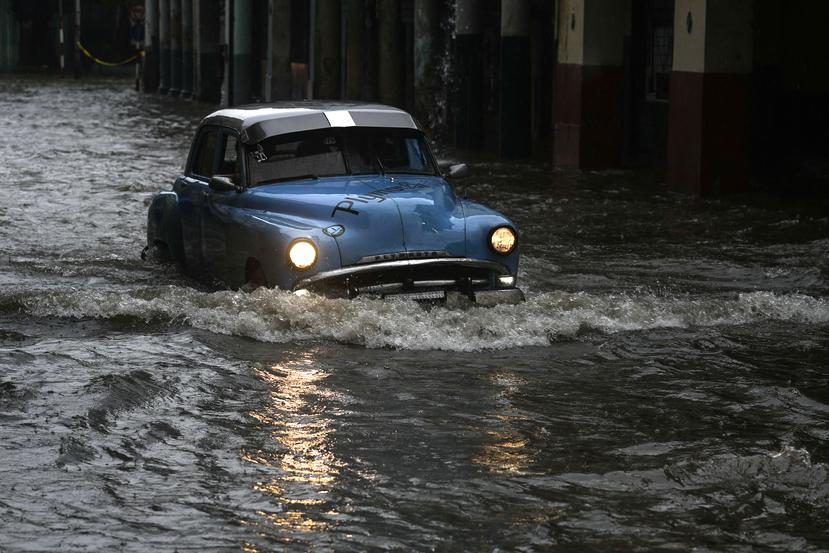 Una persona conduce un automóvil clásico estadounidense por una calle inundada por fuertes lluvias, en La Habana, Cuba, el viernes 3 de junio de 2022.