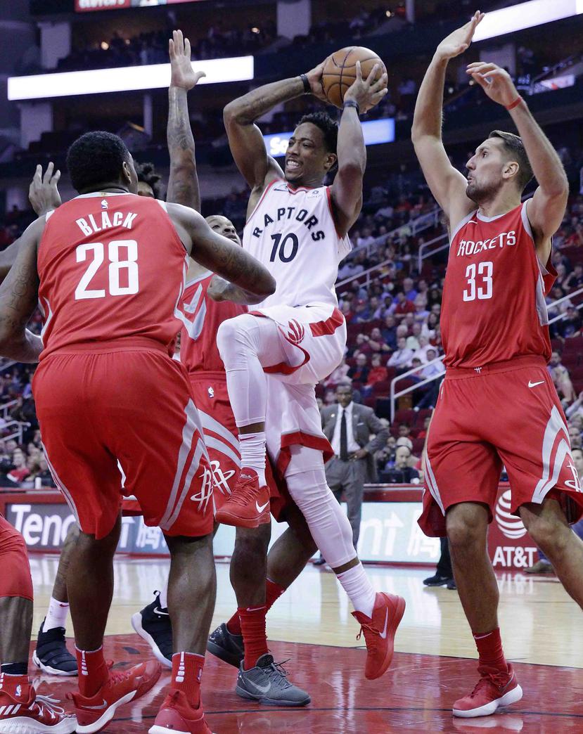 DeMar DeRozan (10) de los Raptors de Toronto trata de anotar en medio de Tarik Black (28) y Ryan Anderson (33) de los Rockets de Houston. (AP /  Michael Wyke)