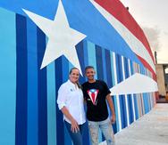 La meteoróloga Deborah Martorell y el artista Héctor Collazo frente a la bandera pintada en la comunidad El Cerro en Gurabo.