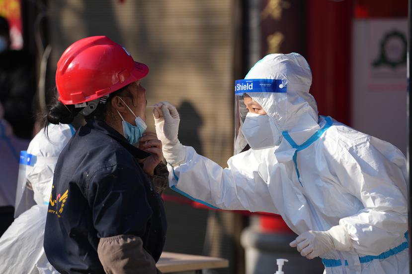 En esta fotografía publicada por la agencia de noticias china Xinhua, un trabajador toma una muestra en un sitio de pruebas de coronavirus, en Xi'an, en China, el martes 21 de diciembre de 2021.