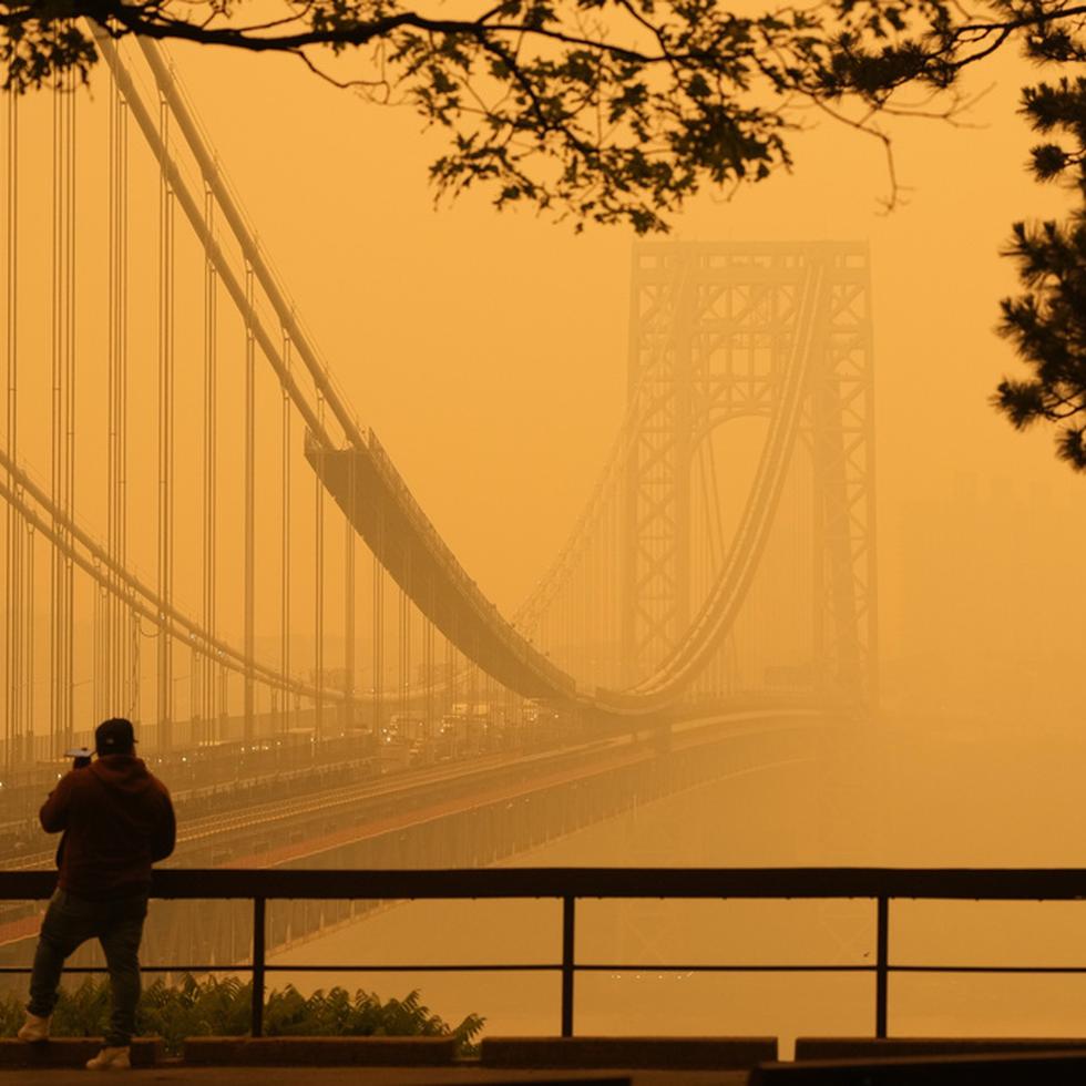 Un hombre conversa por su teléfono en medio de una bruma de humo cerca del puente George Washington, en esta imagen tomada desde Fort lee, Nueva Jersey, el miércoles 7 de junio de 2023. (AP Foto/Seth Wenig)