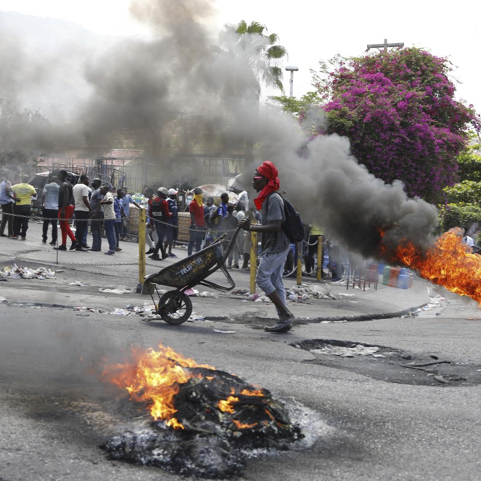 Un hombre empuja una carretilla frente a neumáticos en llamas durante una protesta para exigir la renuncia del primer ministro Ariel Henry, lo que finalmente se materializó.