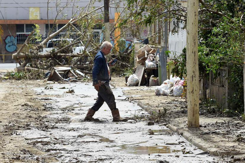 Un hombre cruza una calle llena de fango y escombros en el barrio Buenos Aires en Arecibo.