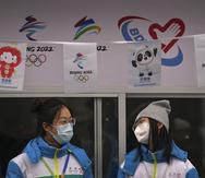 Voluntarias con mascarilla para evitar contagios de coronavirus charlan en un puesto de información para los Juegos Olímpicos de Invierno en la calle de Qianmen, un popular destino turístico en Pekín.