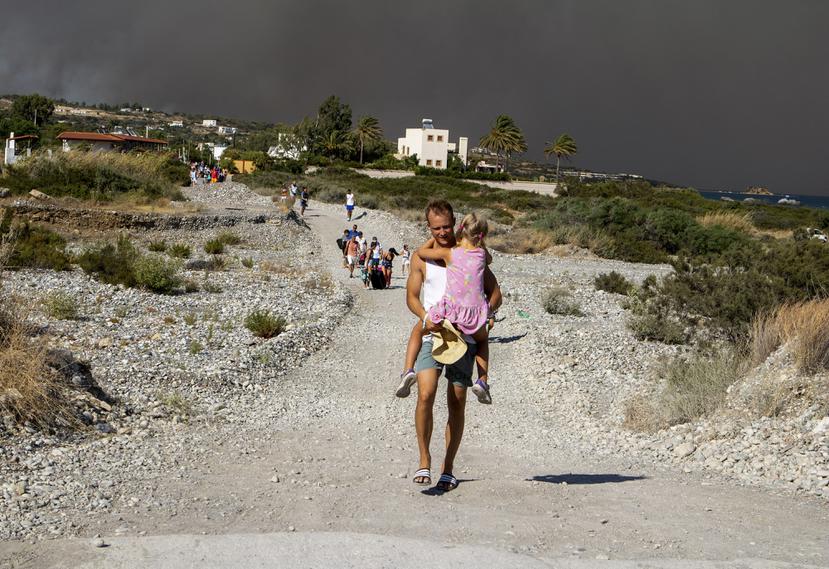 Un hombre carga a una niña al abandonar la zona donde arde un incendio forestal en la isla de Rodas, Grecia.