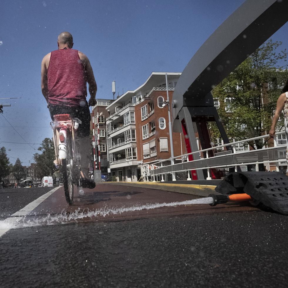 En medio del calor intenso, trabajadores municipales de Ámsterdam echan agua en los puentes sobre los canales para impedir la expansión del metal, que los trabaría y bloquearía el tránsito fluvial.