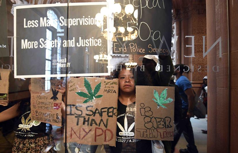 Pilar De Jesús, junto con una coalición de manifestantes, sostiene un letrero exhortando a los legisladores a aprobar la posesión de marihuana contra las puertas del Senado en el Capitolio estatal. (AP)
