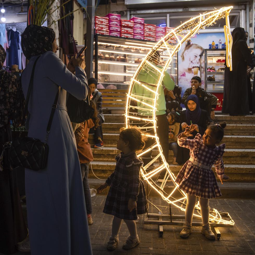 Una mujer toma fotos a su hija junto a una decoración con forma de luna creciente en un mercado, en el inicio del mes sagrado musulmán del Ramadán, en el campo de refugiados de Jebaliya, en el norte de la Franja de Gaza.