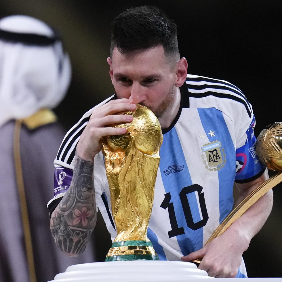 Lionel Messi besa el trofeo de la Copa del Mundo mientras sostiene el premio al mejor jugador del torneo tras la victoria ante Francia en la final.