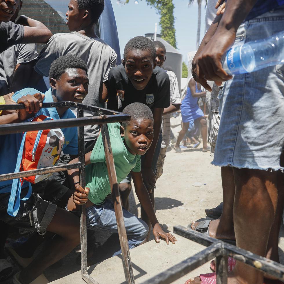Unos jóvenes se agachan tras escuchar disparos en una escuela que sirve de albergue para personas desplazadas por la violencia de las pandillas, en Puerto Príncipe, Haití, el 22 de marzo de 2024.  (Foto AP/Odelyn Joseph)