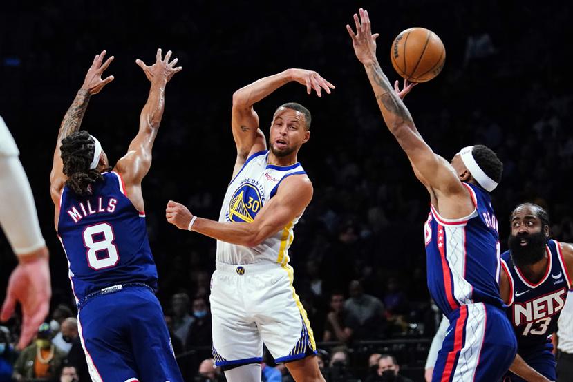 El armador de los Warriors de Golden State, Stephen Curry, realiza un pase mientras es asediado por la defensa de los Nets de Brooklyn.