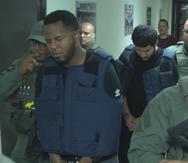 Waldemar Febres Sánchez (con el chaleco antibalas azul) y Edison Merced Olivera (detrás de Febres Sánchez) fueron arrestados en República Dominicana y trasladados a Puerto Rico en febrero de 2019.