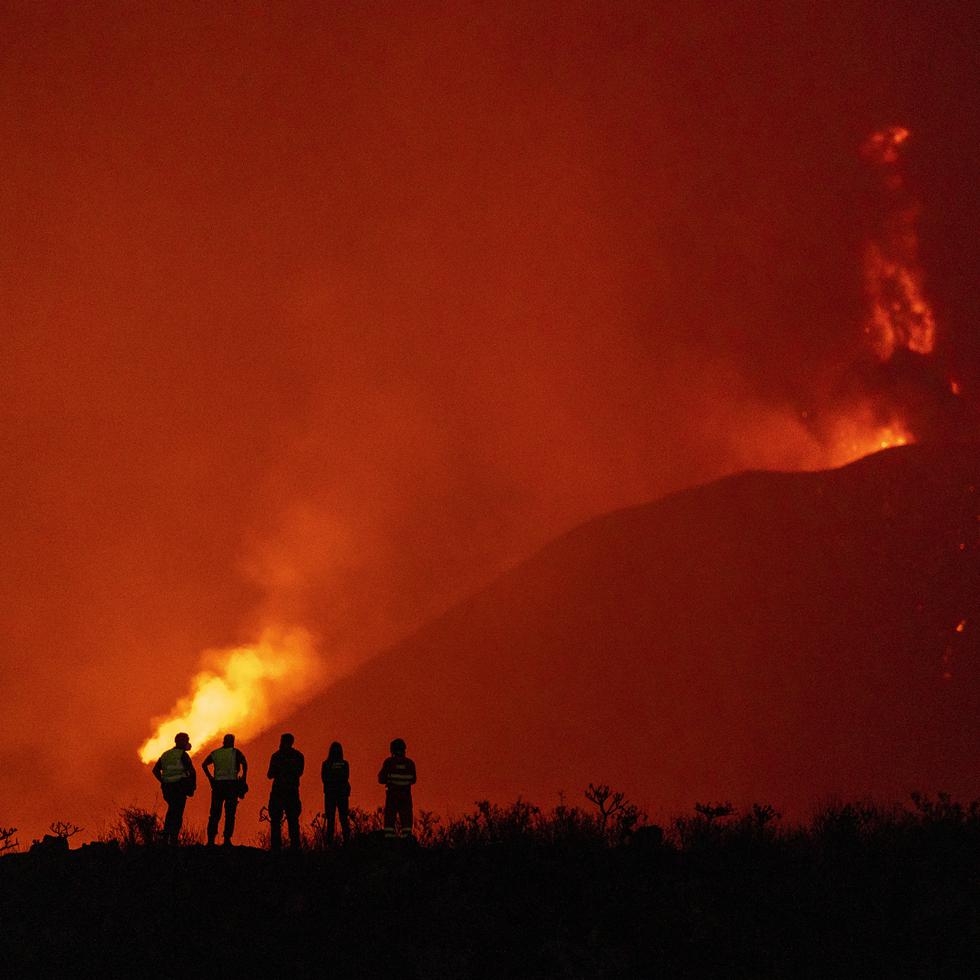 Agentes de policía y personal de emergencias contemplan el flujo de lava de un volcán que continúa en erupción en La Palma, Islas Canarias.