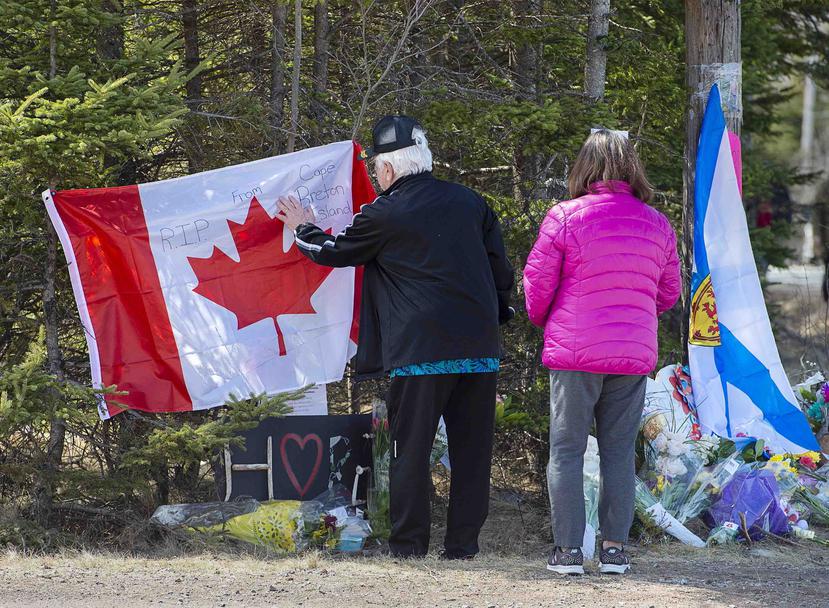 En esta imagen, tomada el 22 de abril de 2020, una pareja coloca una bandera en un monumento improvisado para recordar a las víctimas de una balacera en Portapique, Canada. (AP)