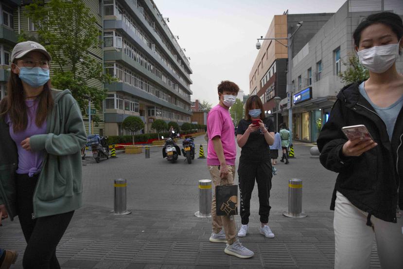 Varias personas cubren sus caras con máscaras como medida contra la propagación del nuevo coronavirus mientras caminan al aire libre por una zona comercial en Beijing. (AP)