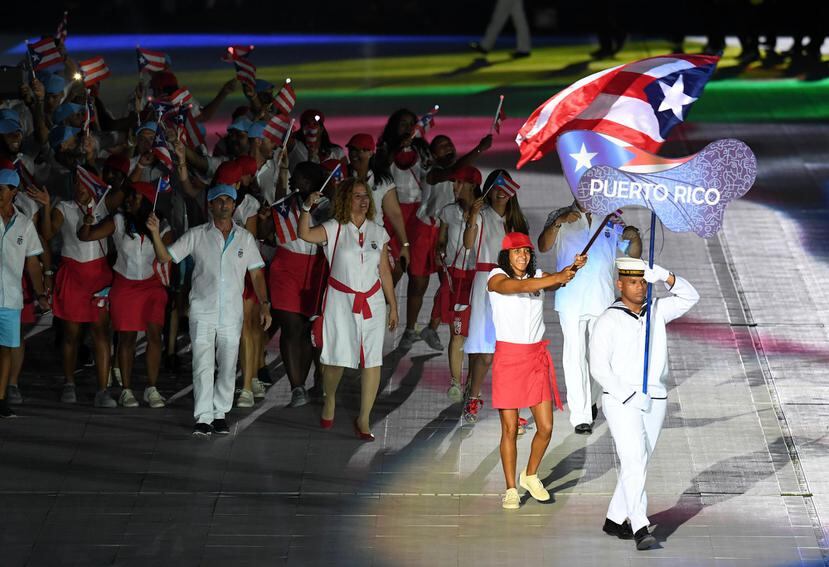 Arriba, la nadadora Vanessa García carga la bandera de Puerto Rico durante el desfile de la delegación en los Juegos en Barranquilla.