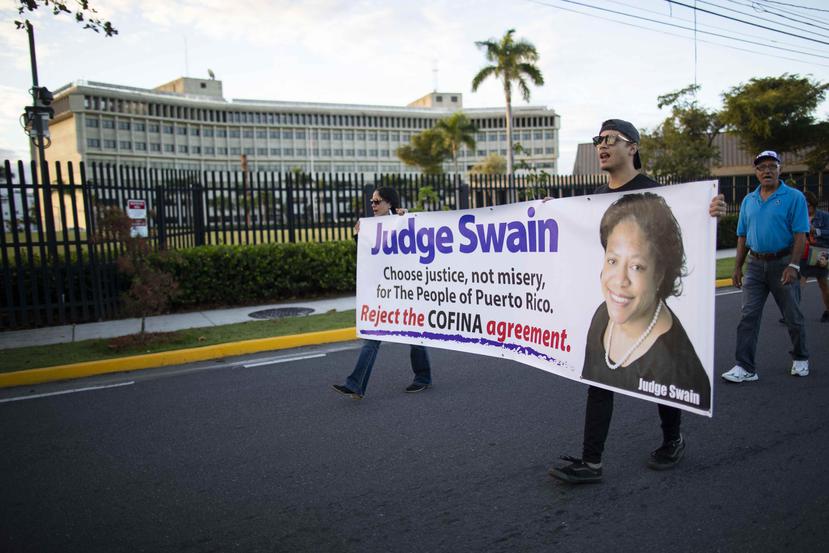 Previo al inicio de la vista que vería la jueza Laura Taylor Swain, cuya foto sale en la pancarta, decenas de manifestantes mostraban su rechazo al acuerdo de Cofina a las afueras del Tribunal Federal en Hato Rey.