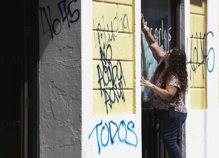 Una persona limpia una puerta luego de una noche de manifestación en el Viejo San Juan.