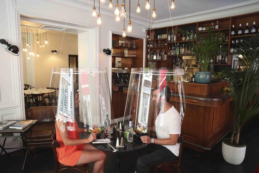 Un hombre y una mujer comen bajo un escudo de plástico el miércoles 27 de mayo de 2020, en un restaurante de París. (AP)