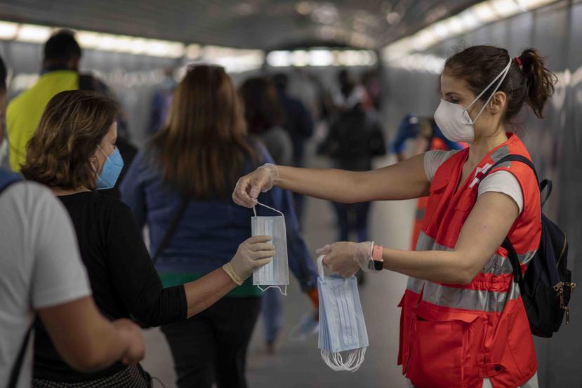 Pasajeros recibiendo mascarillas repartidas por voluntarios de Cruz Roja en una estación de tren de Barcelona, España. (AP)
