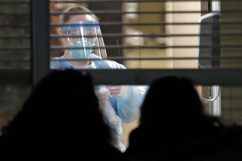 Una trabajadora vestida con una máscara y un traje de protección, vista a través de una ventana en el interior de la habitación de Susan Hailey, de 76 años, quien dio positivo por un nuevo coronavirus. (AP)