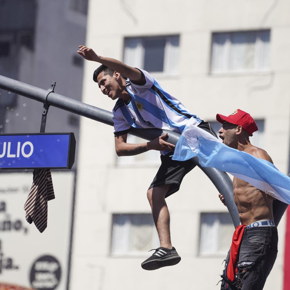 Fanáticos argentinos se subieron a un poste en la conocida avenida 9 de Julio, en Buenos Aires, durante los festejos por la coronación de su equipo en la Copa del Mundo.