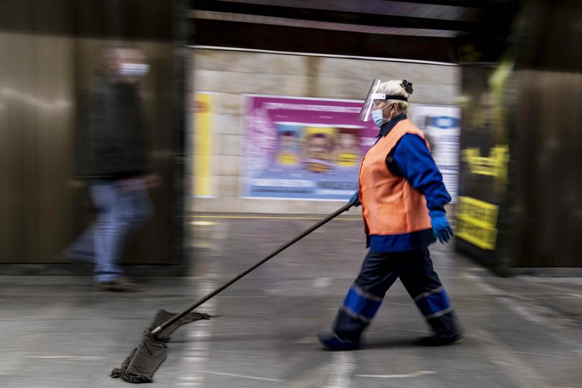 Una empleada con mascarillas y guantes limpia el piso de una estación de metro en Kiev, Ucrania.