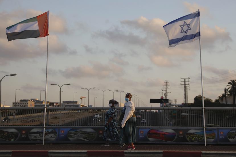 Mujeres con cubrebocas para evitar la propagación del coronavirus pasan entre las banderas de los Emiratos Árabes Unidos e Israel en el Puente de la Paz en Netanya, Israel.