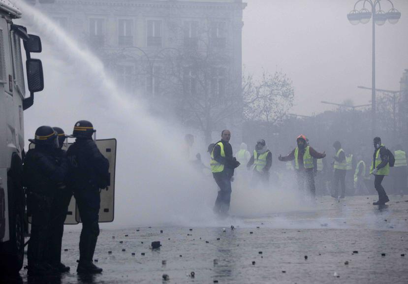Manifestantes vestidos con chalecos amarillos se enfrentan a los cañones de agua de la policía durante una protesta cerca de la avenida de los Campos Elíseos, en París, el 1 de diciembre de 2018. (AP)