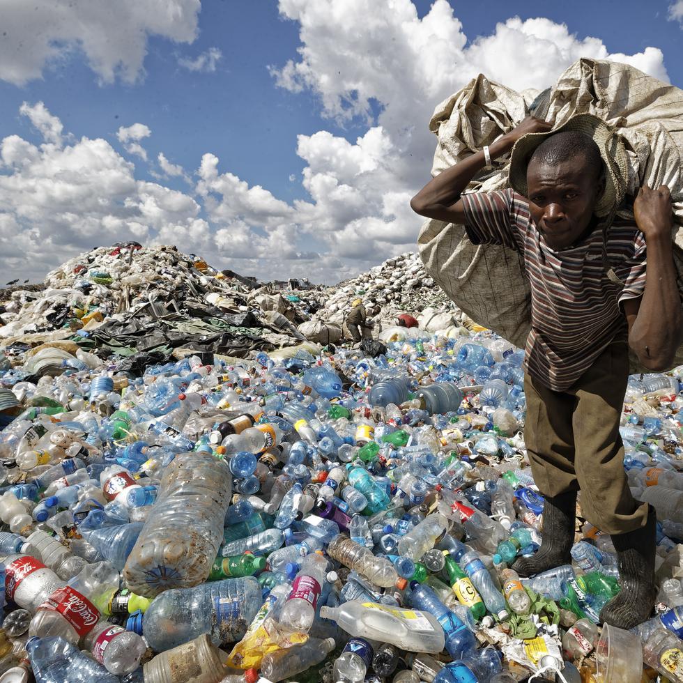 Un hombre camina sobre una montaña de botellas de plástico mientras carga un saco lleno de ellas con el fin de venderlas para su reciclaje, el 5 de diciembre de 2018, en el vecindario de Dandora, en Nairobi, Kenia. (AP Foto/Ben Curtis, archivo)