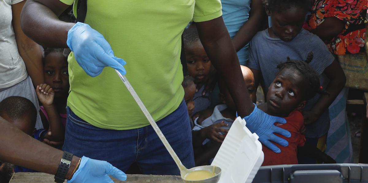 Una persona sirve sopa en un recipiente mientras varios niños hacen fila para recibir comida en un albergue para familias desplazadas por la violencia de las pandillas, en Puerto Príncipe, Haití. (AP / Odelyn Joseph)