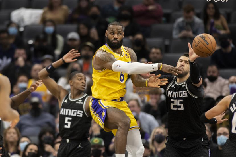 El jugador de los Lakers de Los Ángeles LeBron James pasa el balón mientras los jugadores de los Kings de Sacramento De'Aaron Fox (5) y Alex Len (25) defienden, en la segunda mitad de su juego de NBA en Sacramento, California, el miércoles 12 de enero de 2022. Los Kings ganaron 125-116.
