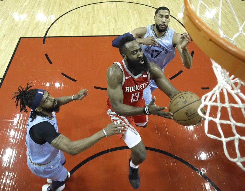 El escolta de los Rockets de Houston, James Harden (13), se cuela hacia la canasta entre los jugadores de los Grizzlies de Memphis, Garrett Temple (17) y Mike Conley, izquierda, durante la primera mitad de un juego de la NBA, el lunes 14 de enero de 2019,