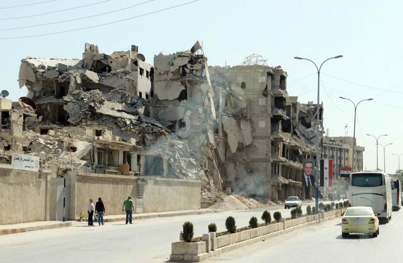 Una fotografía tomada a través de la ventana de un autobús muestra a personas caminando frente a un edificio destruido, en una ciudad no especificada en la provincia de Alepo, Siria. (EFE)