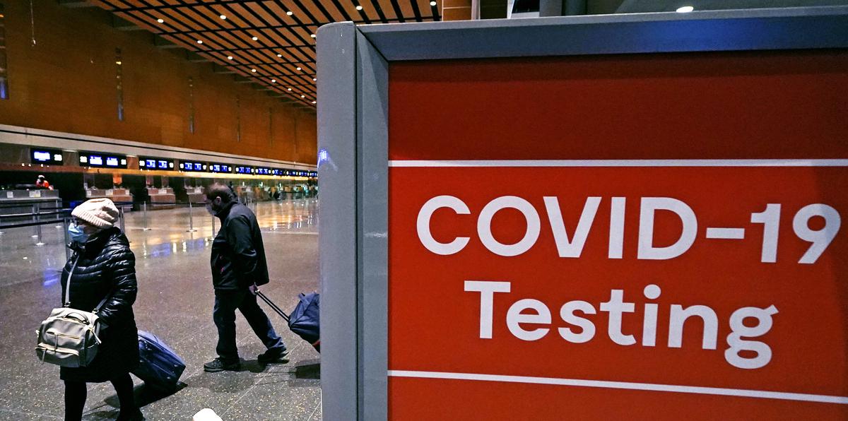 Viajeros pasan junto a un letrero cerca de un centro de pruebas de COVID-19 en la Terminal E del aeropuerto Logan, en Boston.