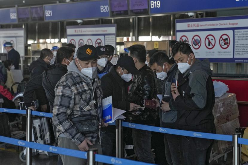 Los viajeros con mascarilla verifican sus pasaportes mientras hacen fila en el mostrador de facturación de vuelos internacionales en el Aeropuerto Internacional de Beijing, en Beijing.