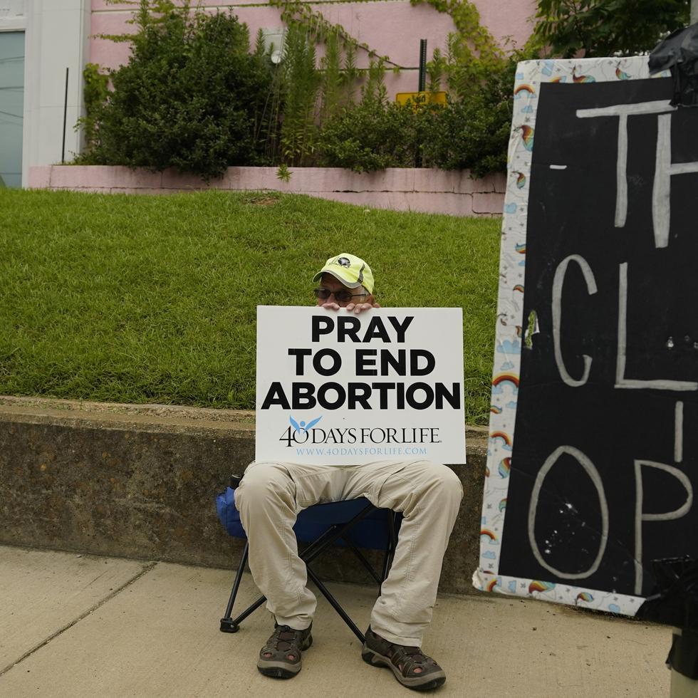 Un opositor al aborto se sienta detrás de un letrero que anuncia que la clínica de la Organización de Salud Femenina de Jackson está abierta, en Jackson, Mississippi.
