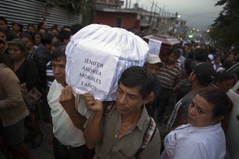 Gente cargando el ataúd de Jennifer Andrea Morales, de tres años, fallecida durante la erupción del Volcán de Fuego, mientras varios vecinos trasladan los cuerpos de siete víctimas al cementerio de San Juan Alotenango, Guatemala. (AP)