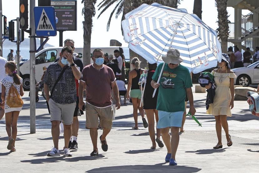 Un hombre se protege del intenso calor con una sombrilla de playa por las calles de la ciudad de Alicante, España.